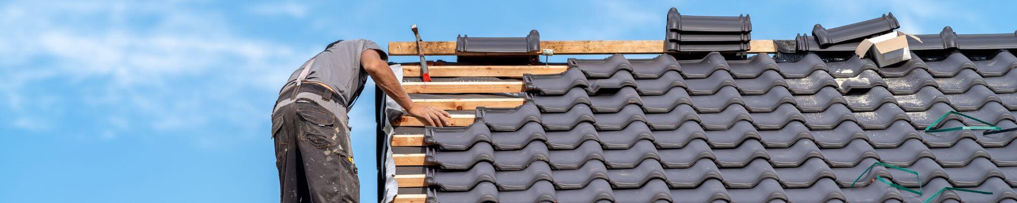 Un couvreur installe des tuiles neuves sur une charpente en bois, lors d’une rénovation de toiture.